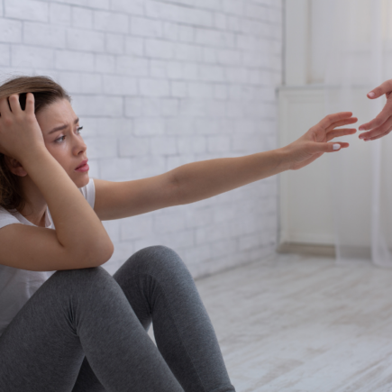 how to support a suicidal friend: a depressed woman sitting on the floor reaching out her hand to another person