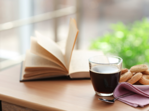 photo of a book with pages being flipped through with a cup of coffee with biscuits on a table