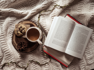 photo of an open book, coffee, and cookie on a blanket