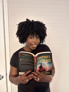 photo of Kathleen Haagenson holding the book vampires of el Norte by Isabel Cañas wearing a black shirt and a smile