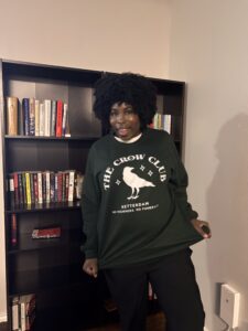 photo of kathleen haagenson wearing a green sweatshirt standing in front of bookshelves