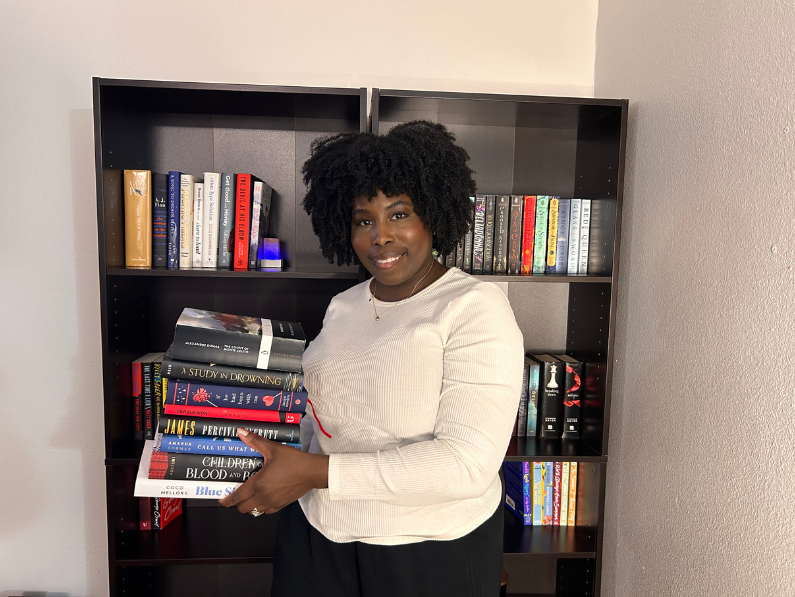 picture of kathleen in front of her home library holding a stack of books for her january tbr 2025
