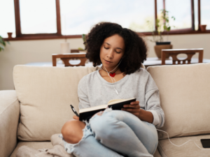 photo of woman writing in a journal while listening to music sitting on her couch