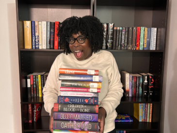 photo of kathleen haagenson standing in front of bookshelves holding 2025 March TBR