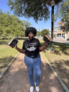 kathleen haagenson wearing a black shirt and jeans holding up library books in both hands