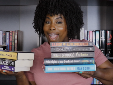 photo of kathleen haagenson holding up books she's considering for her summer tbr 2025