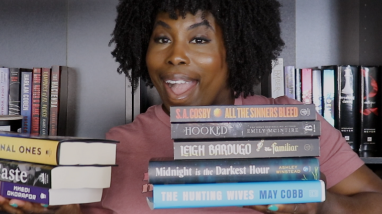 photo of kathleen haagenson holding up books she's considering for her summer tbr 2025