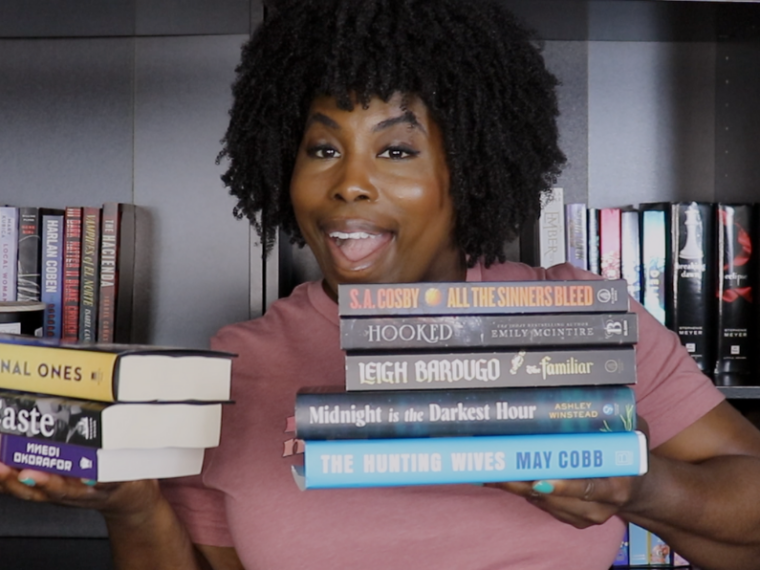 photo of kathleen haagenson holding up books she's considering for her summer tbr 2025