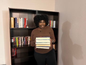 photo of kathleen holding a stack of books in front of a bookshelf