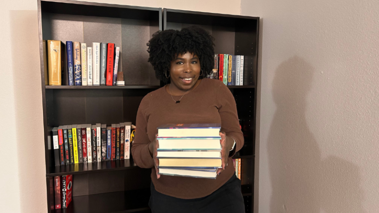 photo of kathleen holding a stack of books in front of two bookshelves nonfiction books about mental health