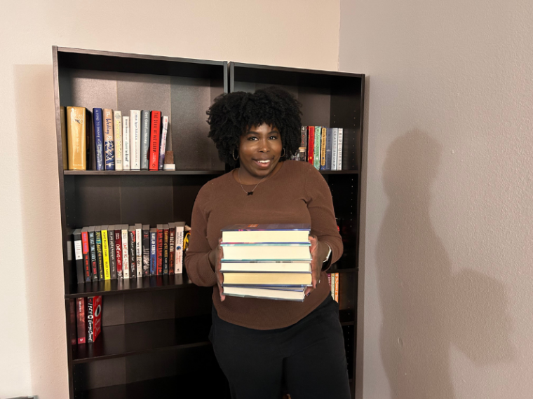 photo of kathleen holding a stack of books in front of two bookshelves nonfiction books about mental health