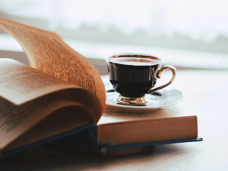 photo of an open book with a cup of coffee sitting on it