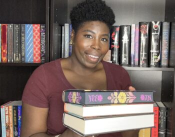 2025 bookish year in review photo of Kathleen holding a stack of books standing in front of her bookshelves